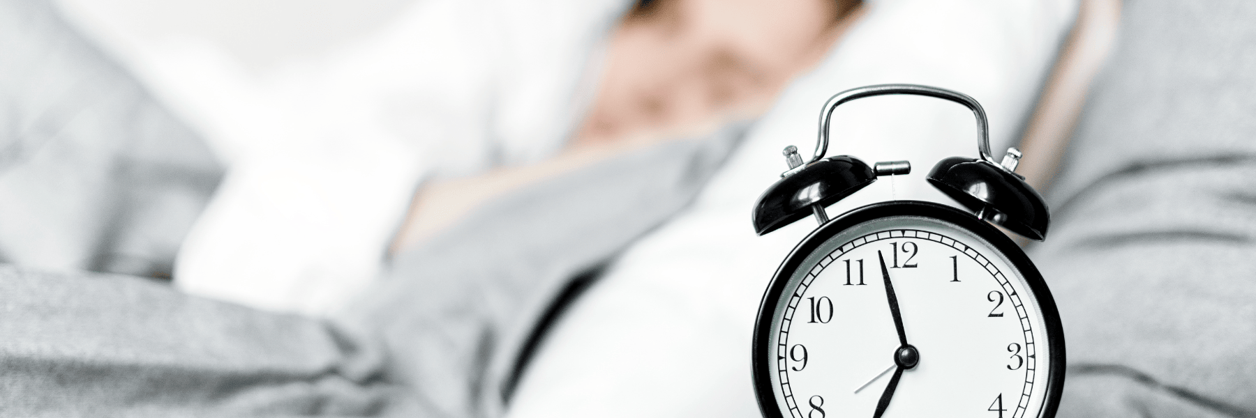 Woman in bed sleeping in background with clock in foreground